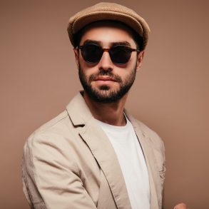 Portrait of man wearing beige jacket, cap and sunglasses on isolated background